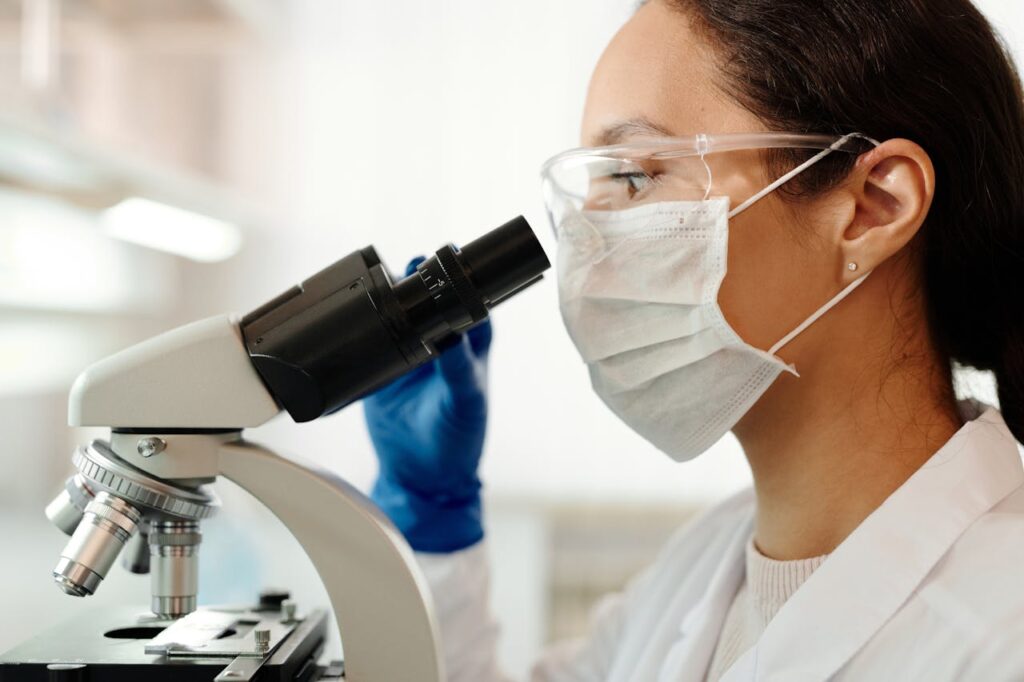 Close-up of a female scientist wearing protective gear and using a microscope in a laboratory setting.
