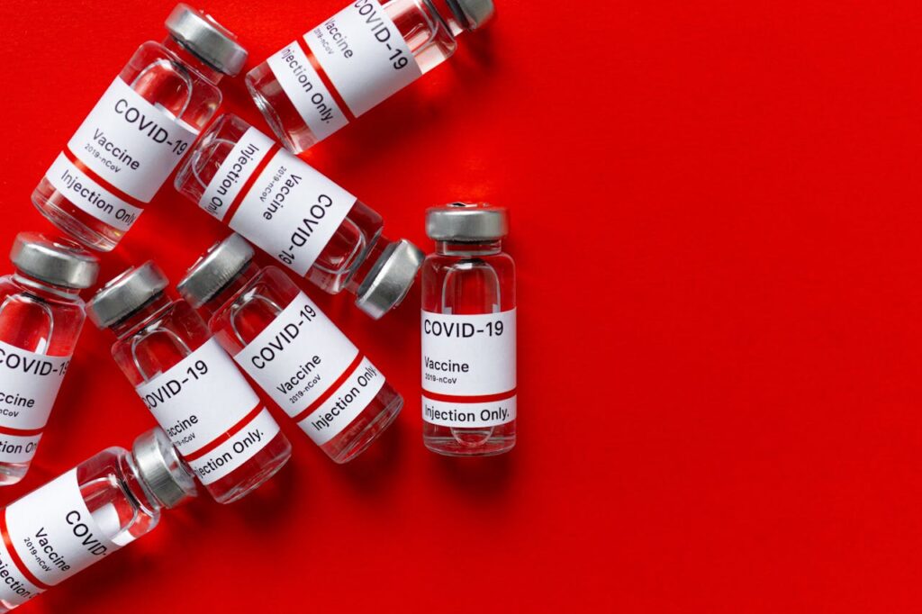 Multiple COVID-19 vaccine vials on a bright red background representing healthcare and vaccination.