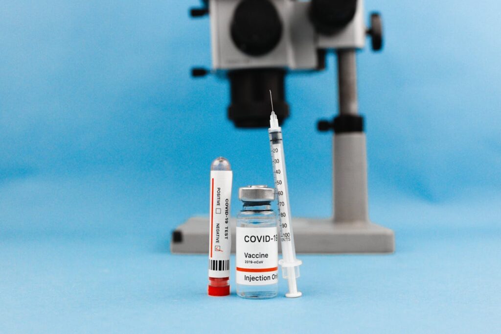 COVID-19 vaccine vial, syringe, test tube, and microscope on blue background, symbolizing research and healthcare.