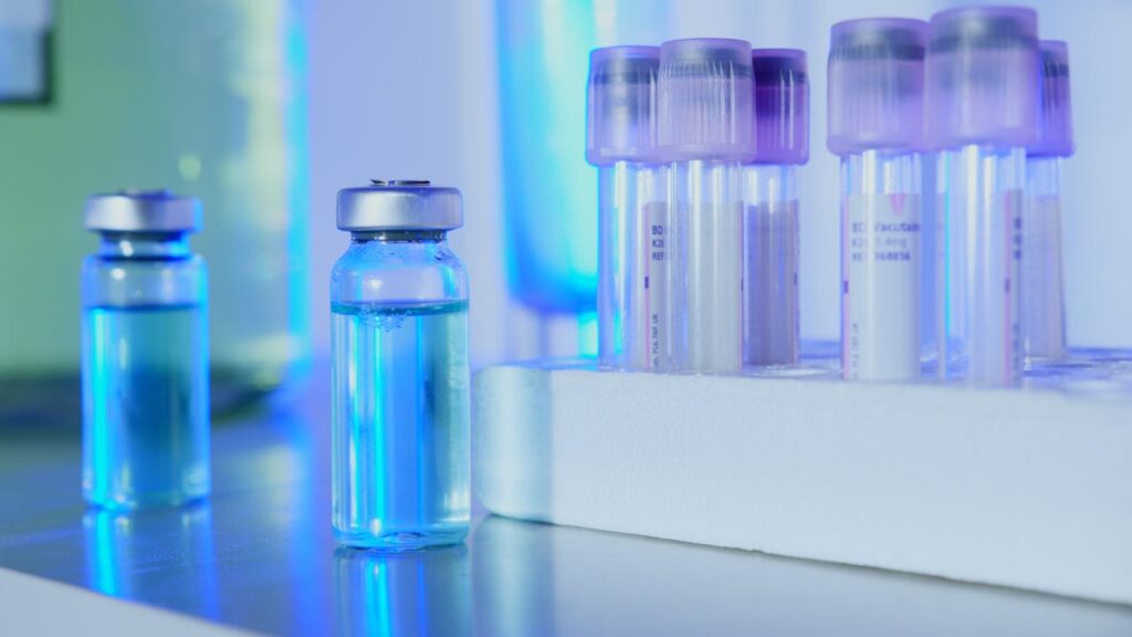 Vials and test tubes with blue liquid in a laboratory setting under fluorescent light.