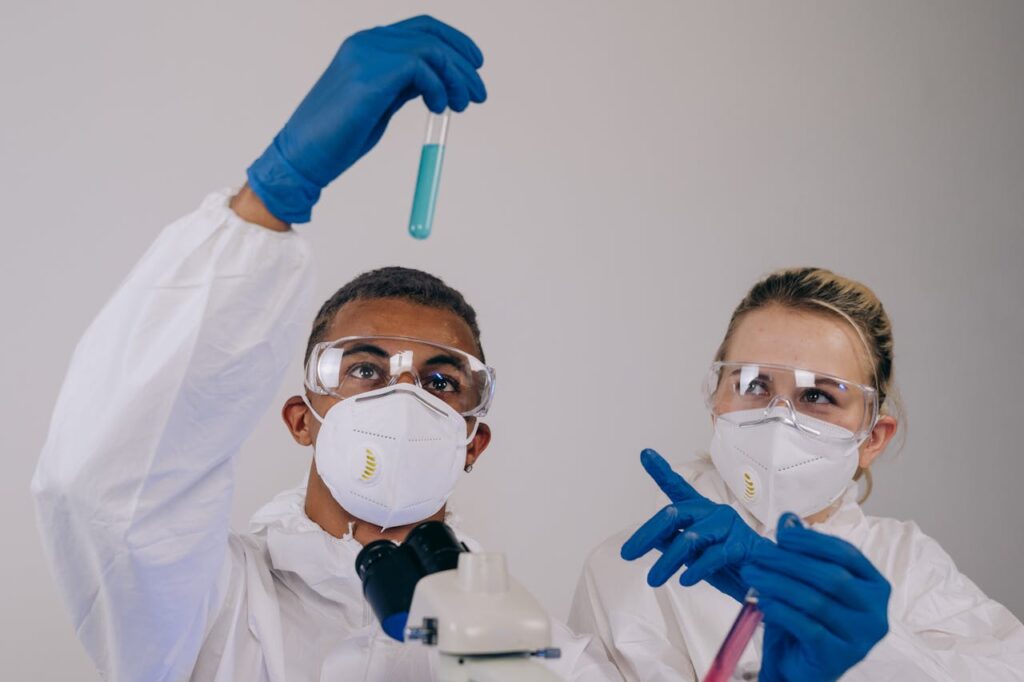 Two scientists in protective gear analyzing test tubes for chemical experiments in a laboratory.