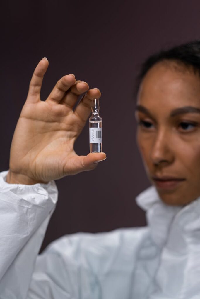 Focused scientist in protective gear examining a vaccine vial indoors.